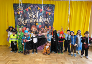 Dzieci przebrane w stroje stoją przed dekoracją karnawałową