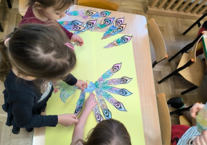 Dzieci układają papierowe pióra wokół sylwety pawia