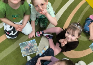 Dzieci siedzą wokół obrazka przedstawiającego dinozaura