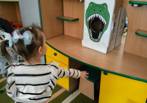 Dziewczynka wrzuca piłkę do pudełka oznakowanego paszczą dinozaura