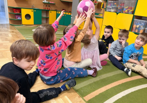 Dzieci siedzą w kręgu i podają sobie piłkę