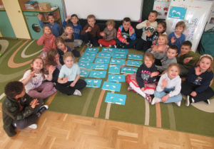 Dzieci siedzą na dywanie, między nimi prace plastyczne - przebiśniegi.