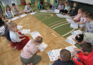 Dzieci siedzą na podłodze w kole, przed nimi leżą książki.