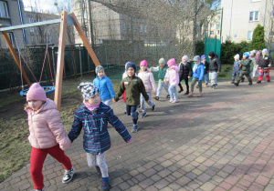 Dzieci maszrują w parach w ogródku przedszkolnym.