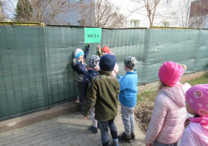 Dzieci stoją w parach, dwóch chłopców pokazuje tabliczkę z napisem meta.