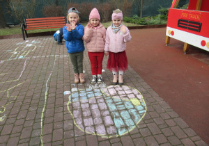 Trzy dziewczynki stoją w ogródku przedszkolnym.