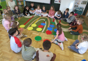Dzieci siedzą w kole podczas zajęć matematycznych, dziewczynka układa krążki.