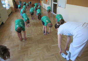Dzieci wykonują skłon podczas zajęć gimnastycznych z elementami taekwondo.