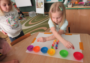 Dziewczynka siedzi przy stoliku i segreguje kolorowe figurki.