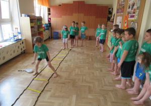 Dzieci ćwiczą z użyciem drabinki koordynacyjnej.