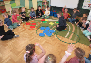Dzieci siedzą w kole, chłopiec układa kolorowe krążki w obręczach.