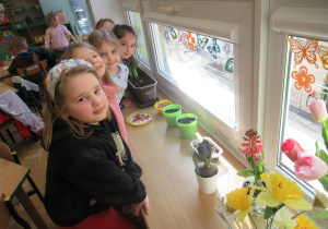 Dziewczynki stoją przy parapecie, na którym jest kącik wiosenny.