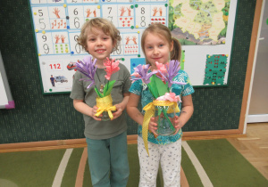 Chłopiec i dziewczynka prezentują kwiaty wykonane podczas warsztatów wiosennych.