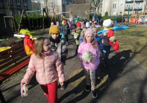 Dzieci maszerują podczas powitania wiosny w ogródku przedszkolnym.