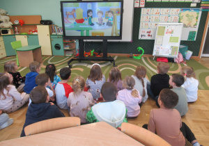 Dzieci siedzą na podłodze i oglądają film o produktach ekologicznych.