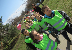 Dzieci idą w parach w odblaskowych kamizelkach.