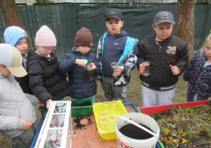 Chłopiec wsypuje ziemię do słoika, pozostałe dzieci stoją wokół.